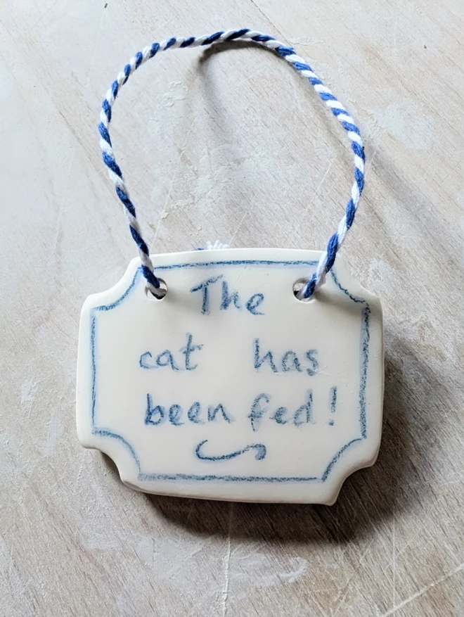 the cat has been fed sign in blue and white ceramic hanging decoration