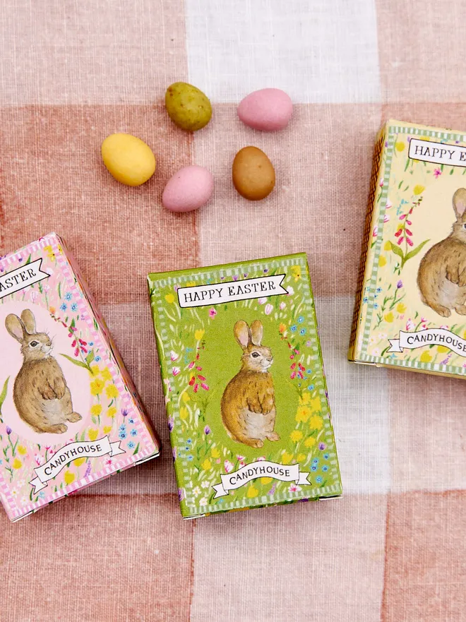Box of three Easter speckled eggs in colours of a green box, a yellow box and a pink box all with a bunny rabbit on the front, placed on a pink and white tablecloth 