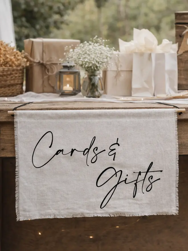A linen cards and gifts banner hanging from a rustic wedding gift table.