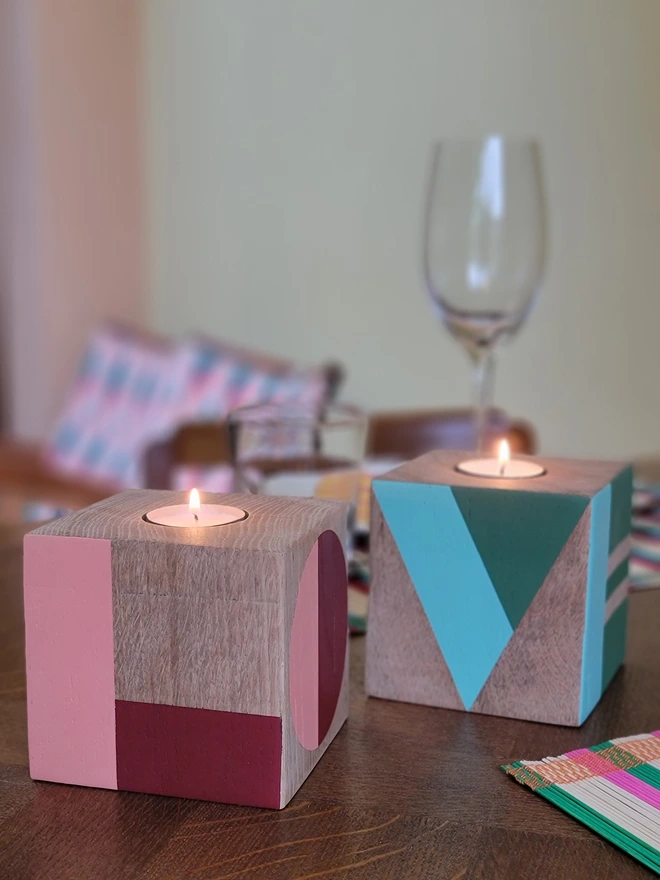 Two wooden painted cubes with tealights on a table, painted pink and red, green and mint with the word LOVE