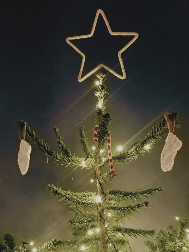 Christmas tree topped with a large string wrapped wire star against a grey background