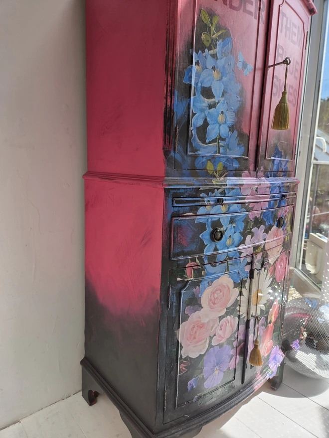 Side view of painted vintage wooden cabinet with pink, blue and floral decoration