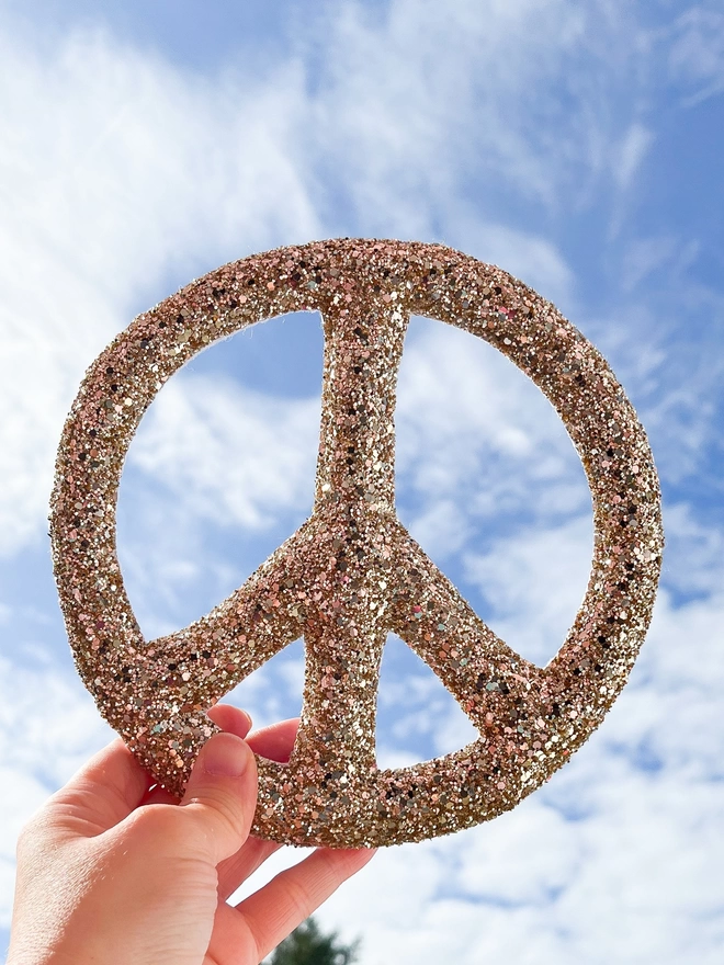 Gold glitter peace sign being held up against a blue sky