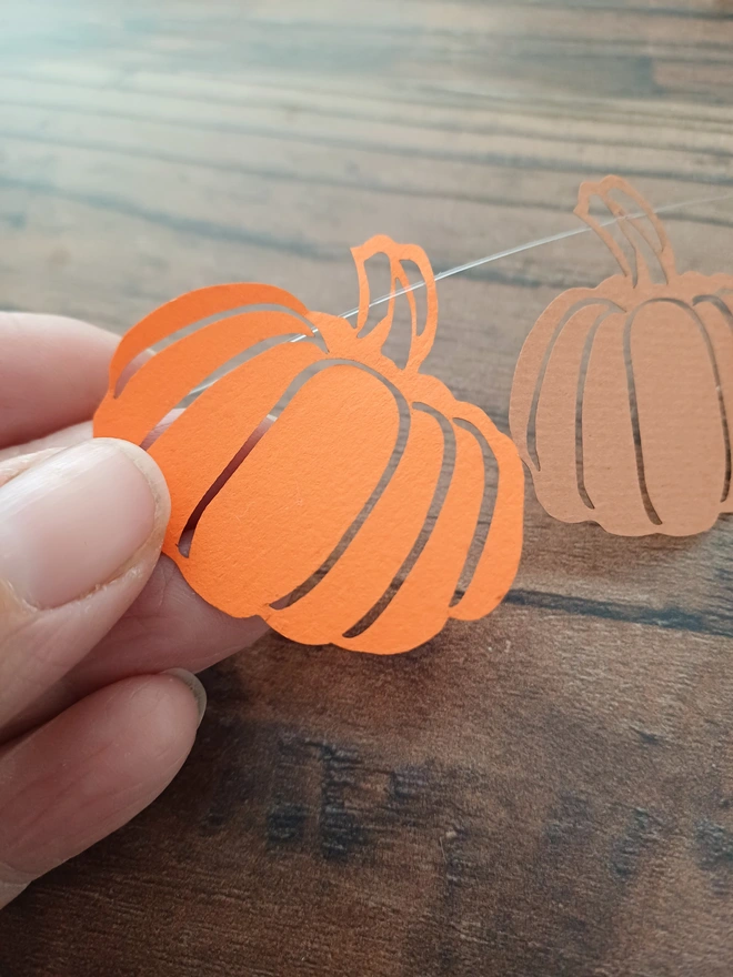 Closeup of orange papercut pumpkin decoration held between designer's thumb and forefinger