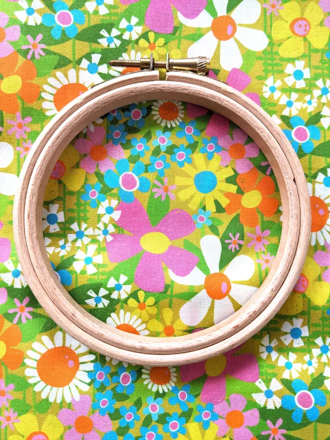 A wooden embroidery hoop lying on fabric with a colourful retro flowers design