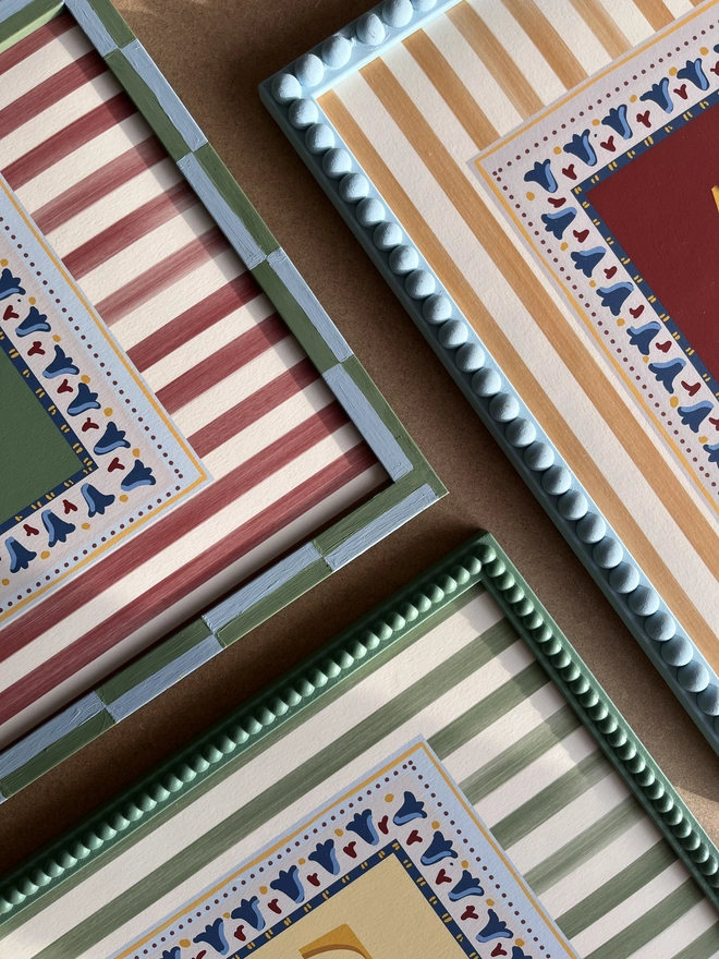 Close-up of Annabel Wond Interiors’ personalized stripy letter prints in custom-painted decorative frames, featuring hand-painted vertical stripes, colorful borders, and bold initials—ideal for children’s room and nursery wall art.