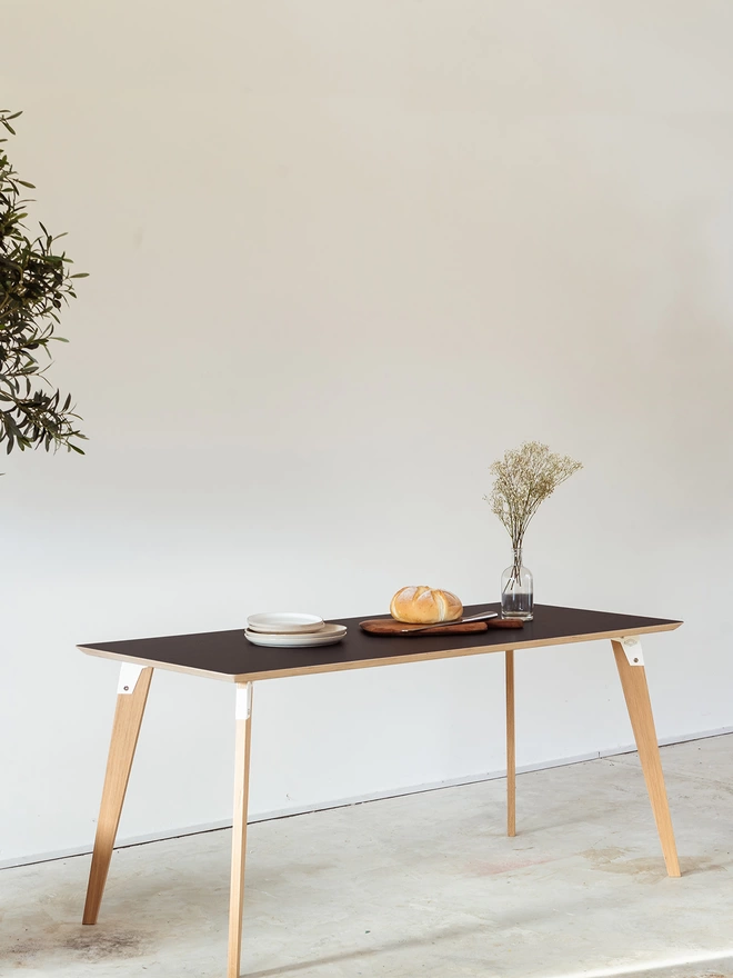 A stylish and minimalist dining table with Fenix top, coloured steel brackets and solid oak legs, set for a simple lunch.