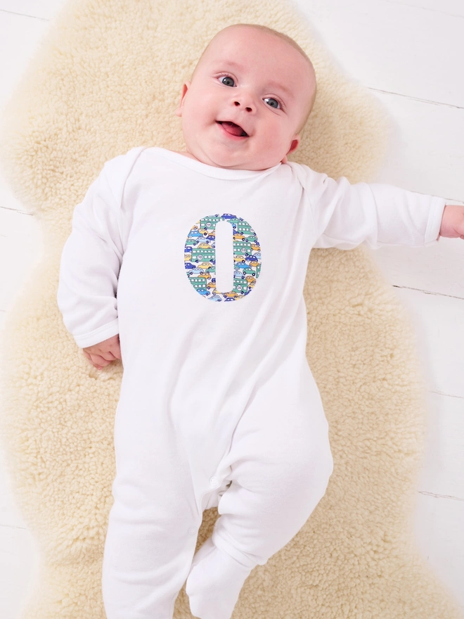 a baby boy in a personalised romper with an initial in Liberty print on the front