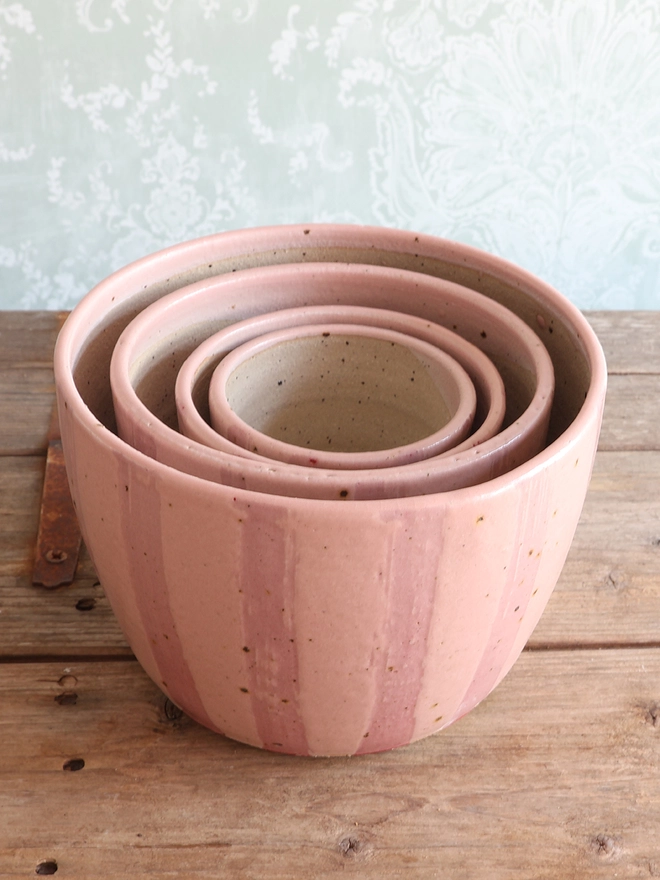 Set of 4 Handmade Ceramic Stoneware Plant Pots in Pink Stripe stacked inside each other on a wooden surface. 