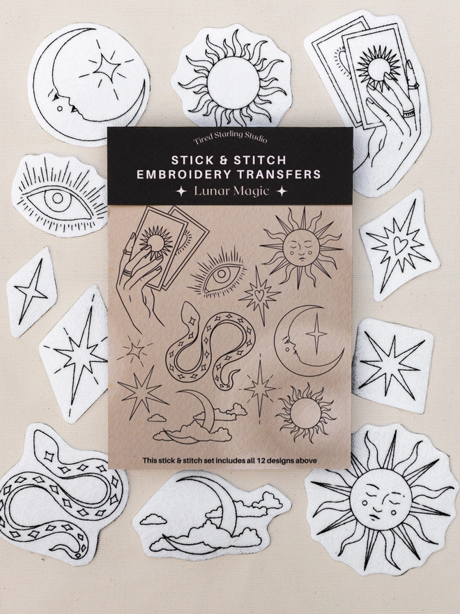 Lunar Magic stick and stitch embroidery transfer set featuring 12 celestial designs including suns, moons, stars, tarot cards, an eye and a snake displayed on a neutral fabric background.