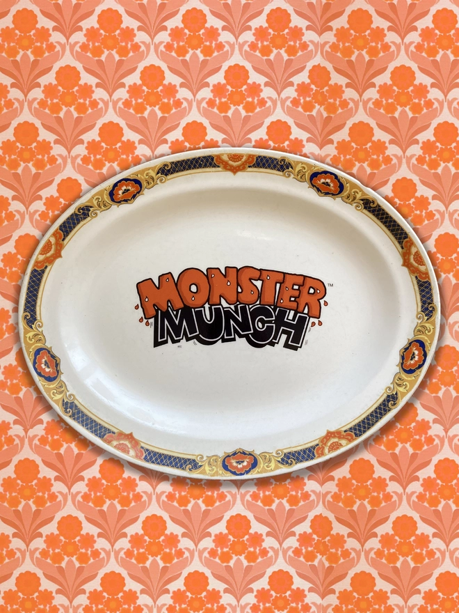 oval shaped vintage plate with the 'Monster Munch' logo in the centre. The rim of the plate is orange and dark blue, and the logo has been created to reflect these colours.