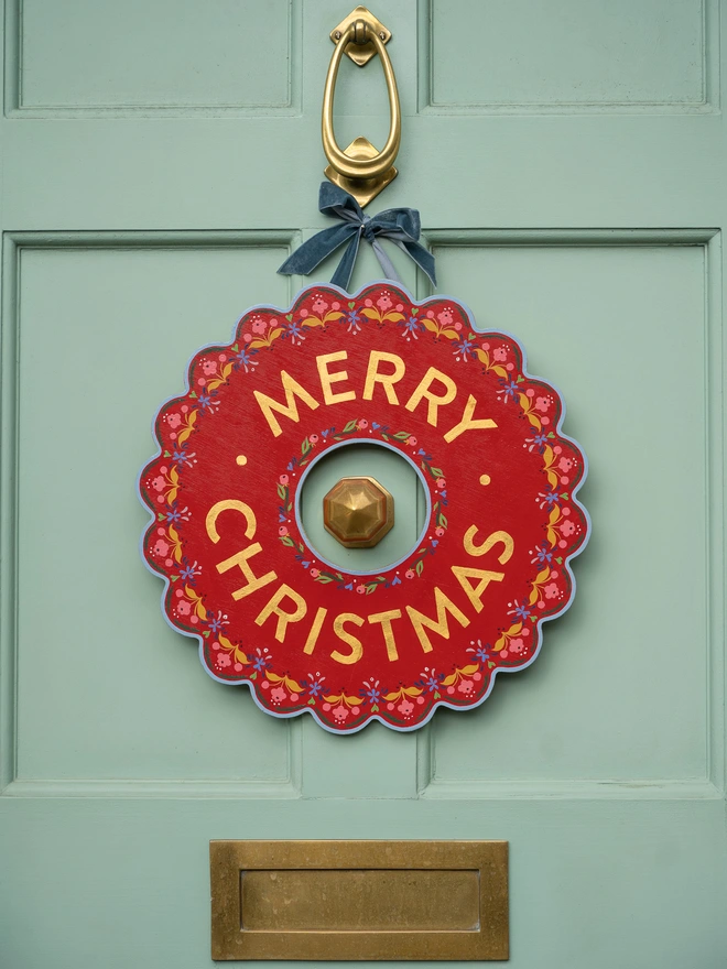 Red Hand painted Christmas Wreath with red lettering and gold leaf lettering on a pale green front door