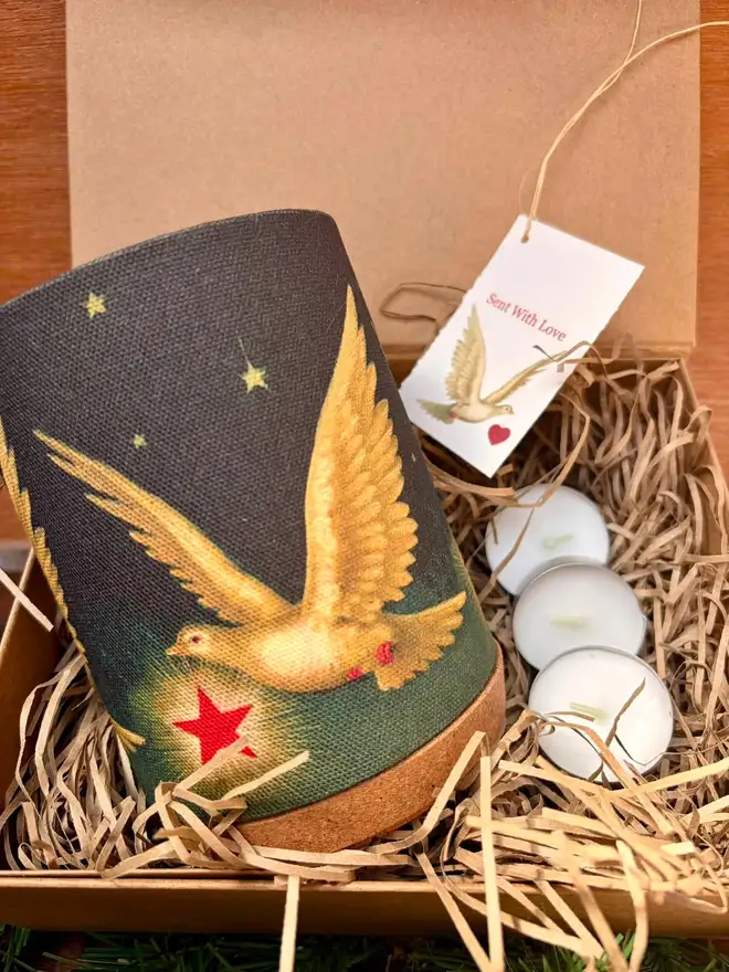 A decorative candle lantern in a gift box with paper straw , tealight candles and a gift tag