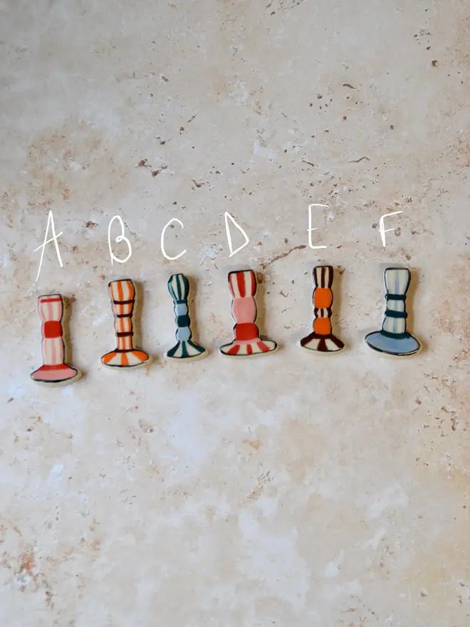 Handmade ceramic candlestick magnets — mix of red, blue and brown striped designs labelled A–F