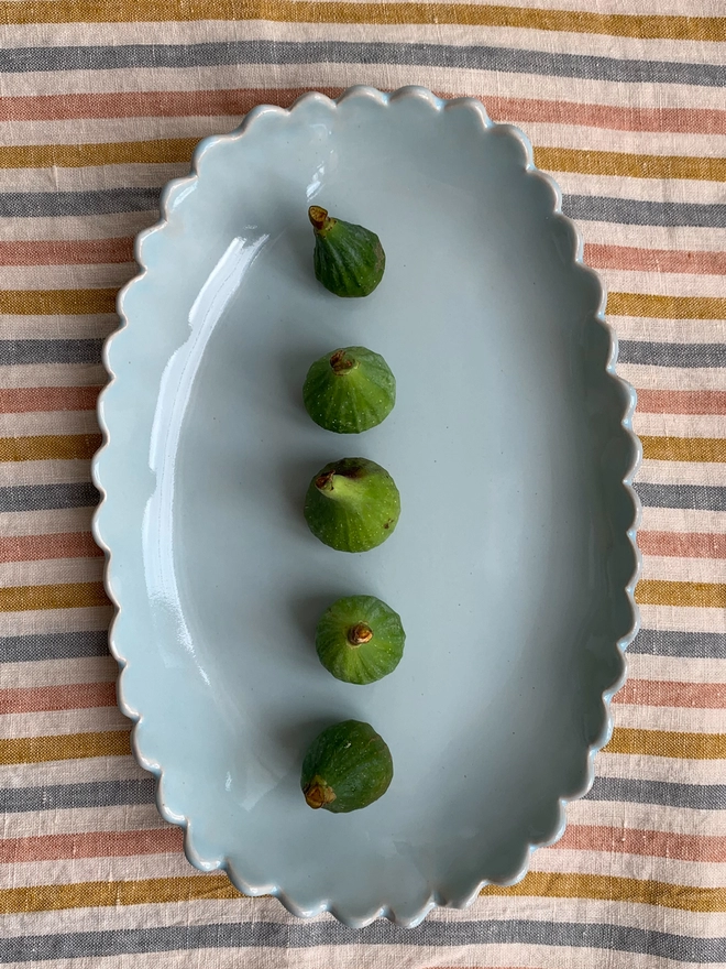 heavne blue oval serving bowl with figs on surface on a pastel striped cloth