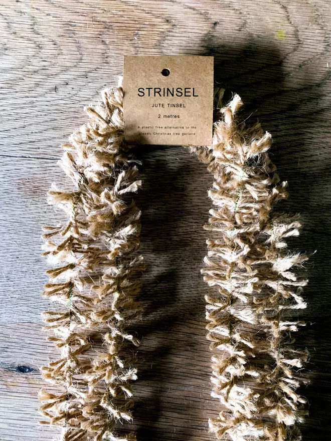 2 metre length of golden undyed jute Strinsel (plastic free string tinsel) with label on oak table