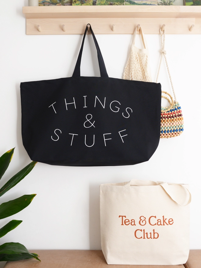oversized black canvas tote bag with things and stuff slogan hanging on a wooden hook