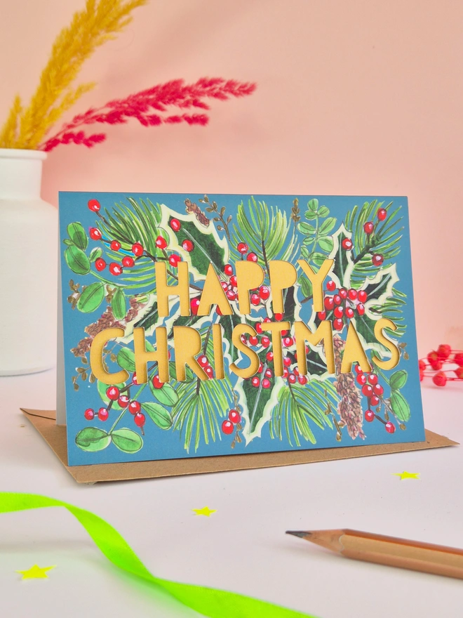Holly illustration Christmas card with paper cut text and pearlescent gold backing paper 
