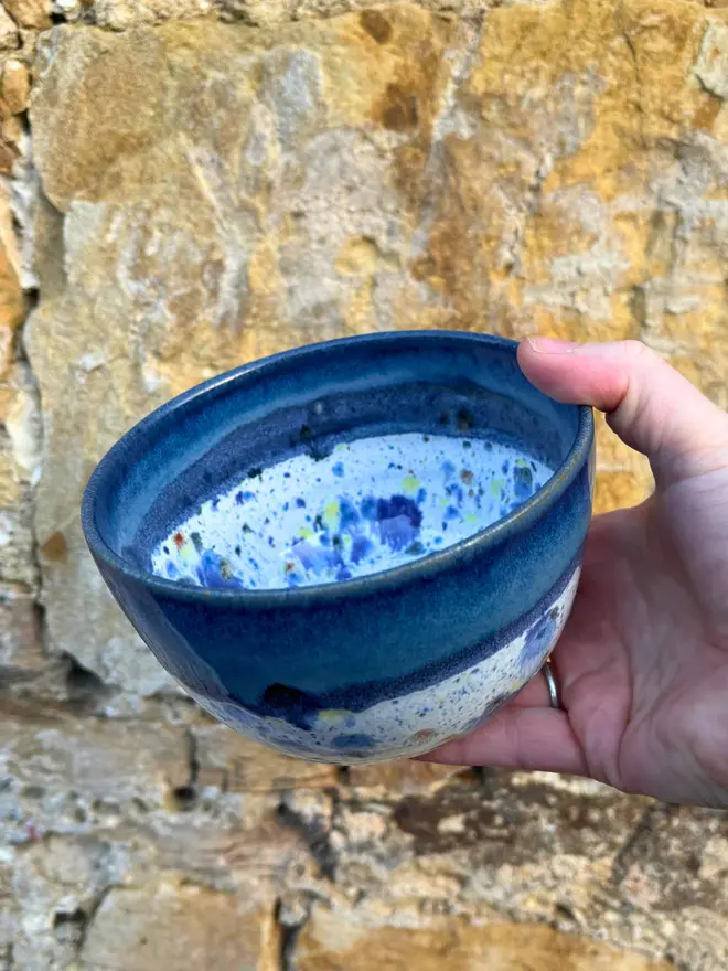Shoreline Small Bowl, a colourful bowl held in front of a brick wall. 
