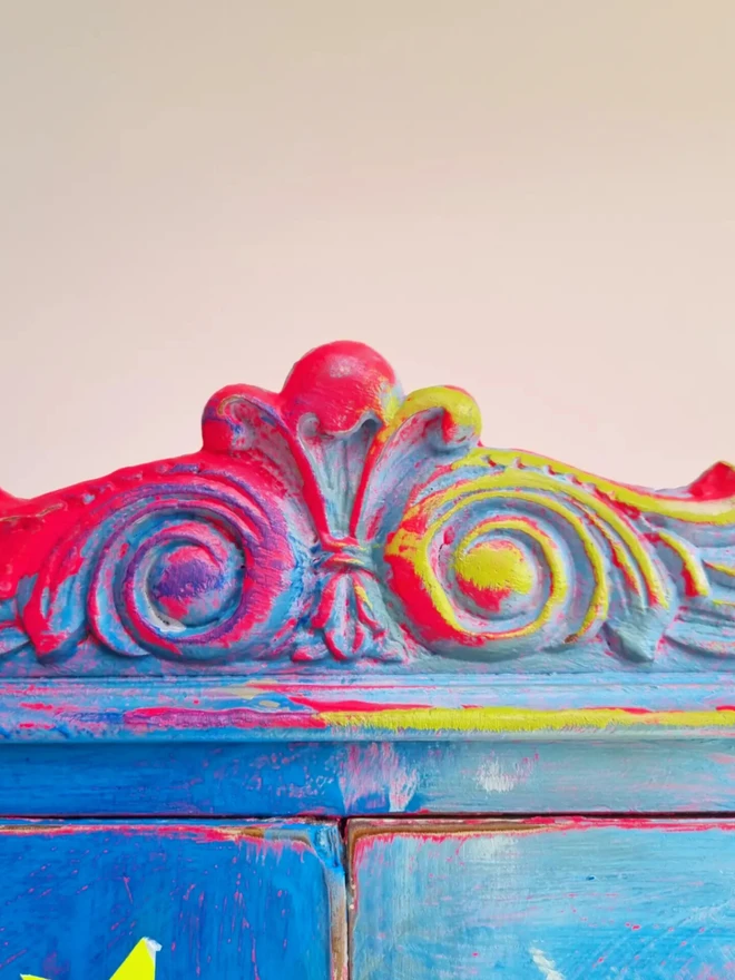 Upcycled cocktail cabinet in neons and bright colours. The decoration features a retro pin-up model on a boat and florals with stars and the wording reads ‘let your heart sing’