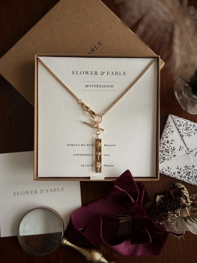 Gold plated sterling silver watch chain with a bar pendant to represent motherhood in a presentation box with language of flowers meanings and flower and fable puzzle purse 