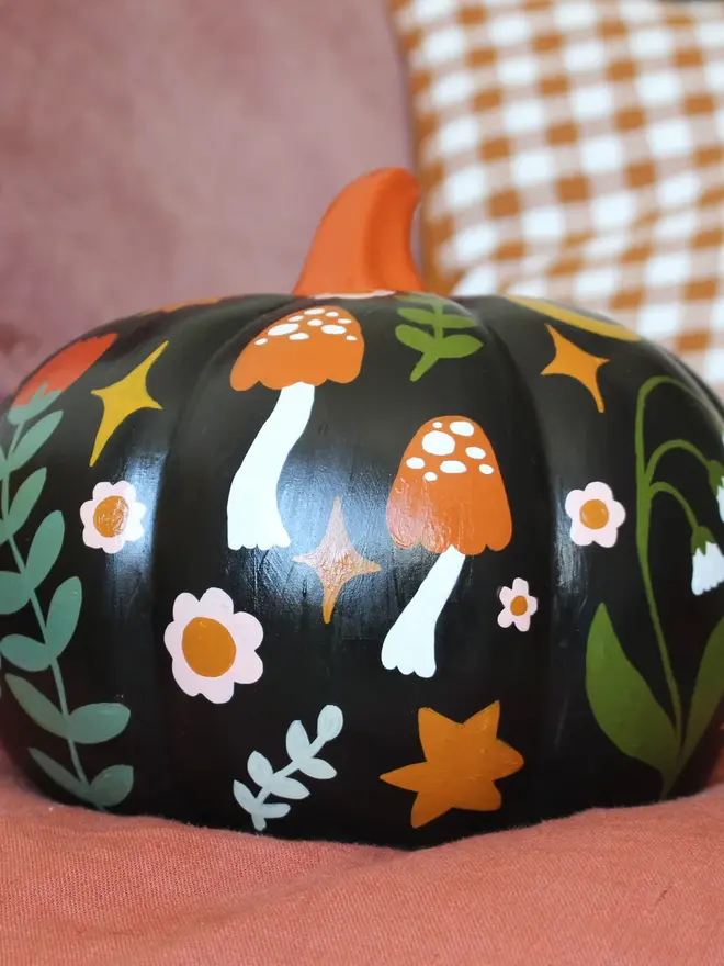hand-painted folk art ceramic pumpkin. a black ceramic pumpkin painted with mushrooms and flowers.