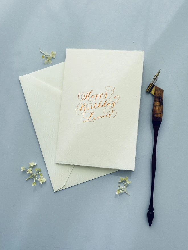 Calligraphy birthday card with envelope next to a calligraphy pen