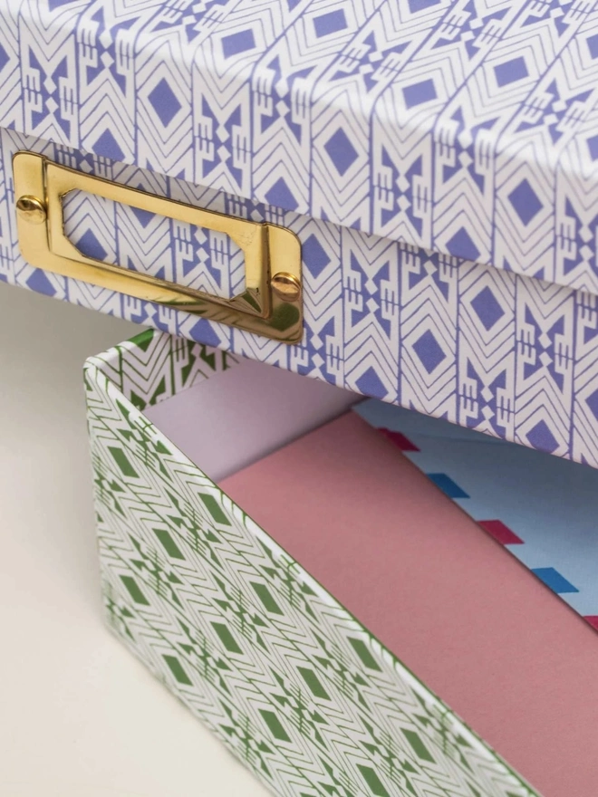 Tijan Lidded Portfolio Box, a collection of colourful portfolio boxes stacked on a plain surface. 