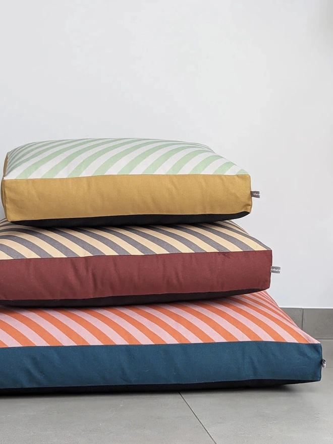 Printed Cotton Patterned Dog Bed, a stack of three dog beds sitting on a floor by a white wall. 