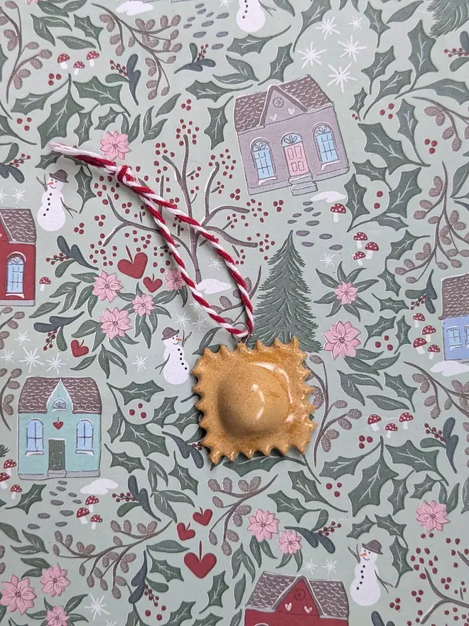 ceramic ravioilini christmas decoration. a small pasta ornament hanging from red and white thread.