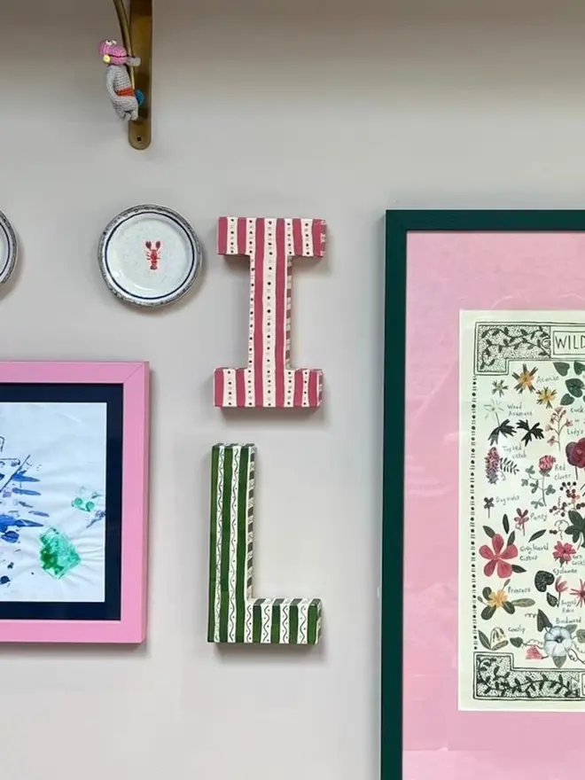 letter I and L hanging on a wall, with other framed art, to show relative size