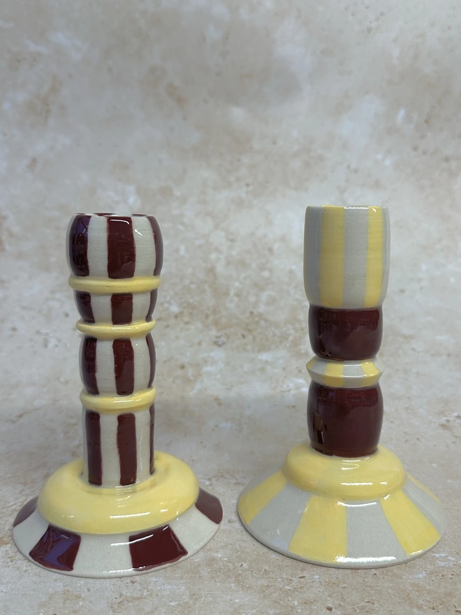 Close-up of two handmade striped ceramic candlestick holders showing stacked shapes and glossy glaze details in yellow and burgundy tones.