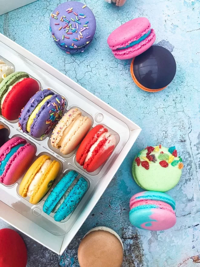 an assortment of colourful macarons in a  white gift box with a colourful illustrated sleeve featuring macarons and other sweet treats