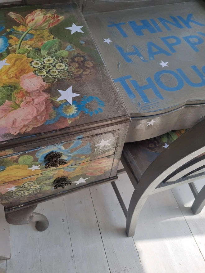 Vintage painted dressing table and chair. Painted in coffee grey and decorated using layered antique florals with yellow and blue accents and finished with hand-cut white paper stars. Text reads in blue 'think happy thoughts'. Heavily distressed finish.