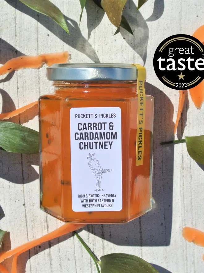 carrot and cardamom chutney. a jar of carrot and cardamom chutney photographed against a wooden background.