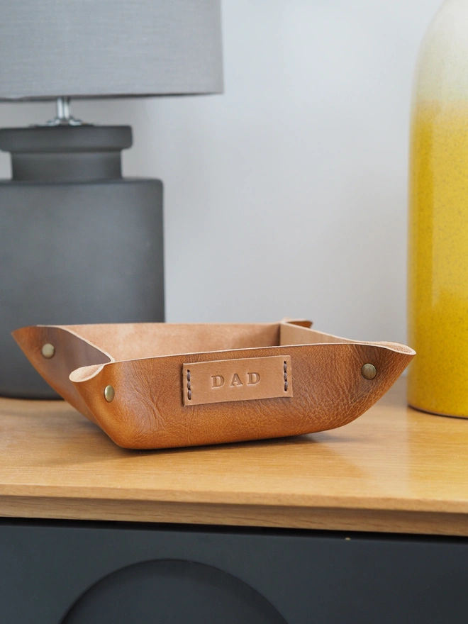 Leather Gift for Dad. Handmade leather coin tray. A square dish sitting on a table, personalised with the name tag DAD.