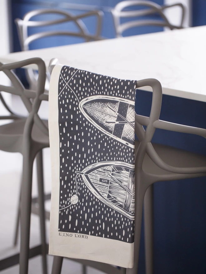 Picture of a tea towel in a kitchen with an image of 3 rowing boats, taken from an original lino print