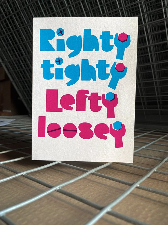 The words Righty tighty screen printed in the colour cyan above the words Lefty loosey printed in magenta. The letter Y at the end of each word is shaped like a spanner. Inside the spanners are hexagon shaped bolts. Overprinted philips screw heads make up the dots of the letter i in righty and tighty and overprinted lines make the o’s in loosey look like standard slot screws. The card is stood on a drying rack.