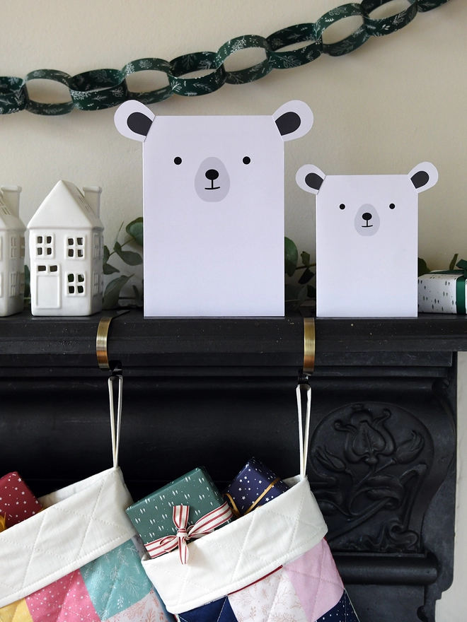 Two white polar bear greetings cards stand on a black mantlepiece where two patchwork stockings are hanging from.