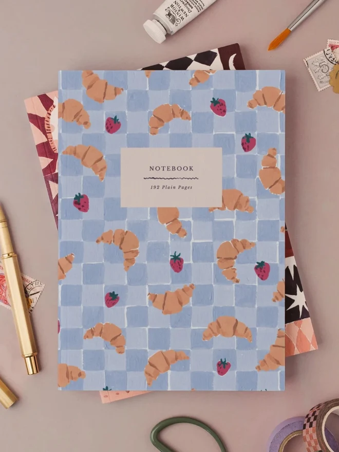 Croissant Cafe Notebook with a gold pen and art supplies