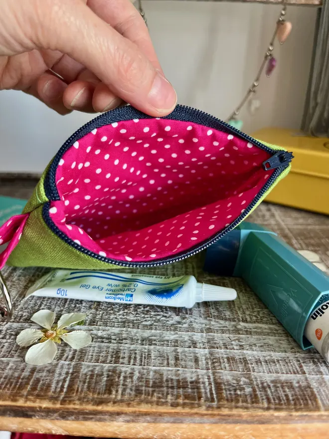 A green coin purse with zip open showing pink polka dot lining.