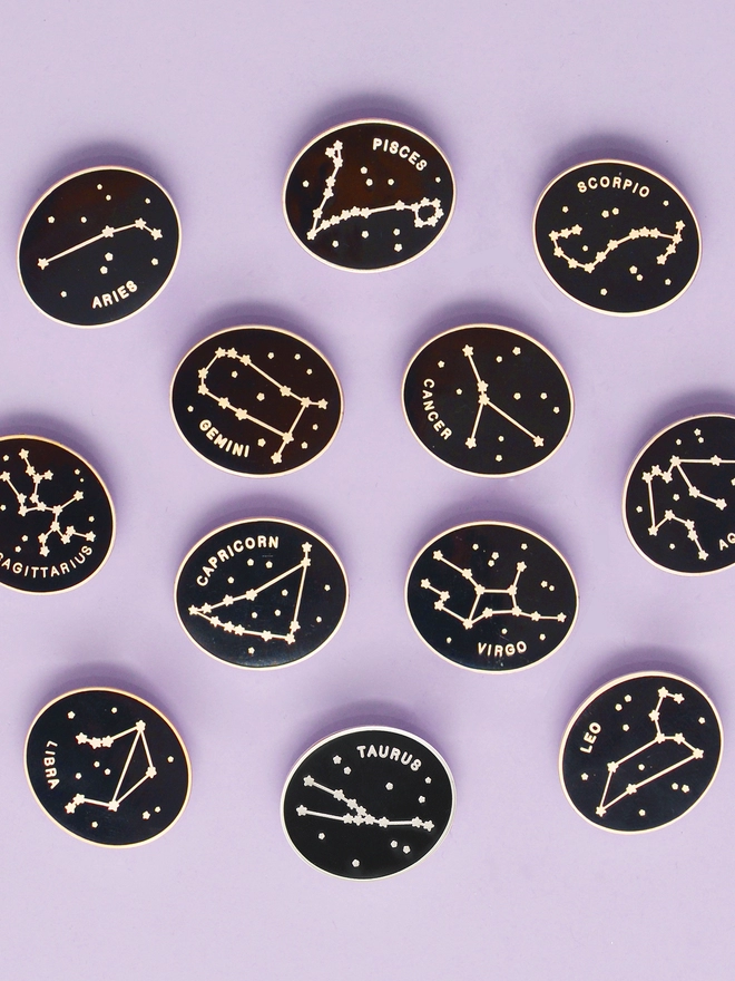 Zodiac enamel pin badges laying on a purple background