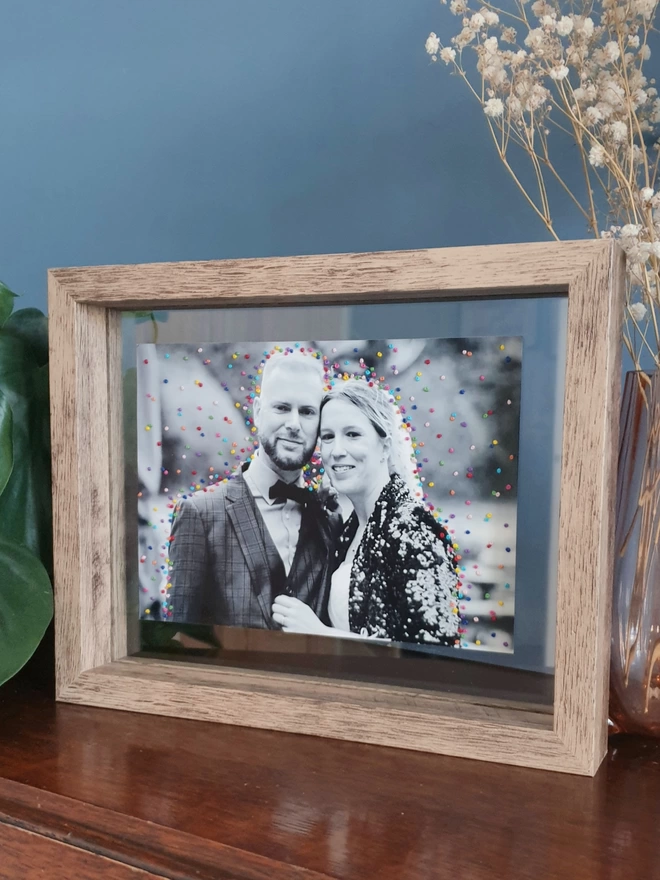 Wedding photo with hand embroidered confetti framed in double glass frame on desk