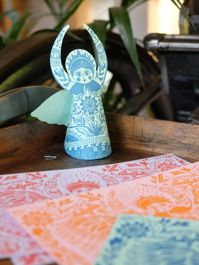 Blue handprinted 3D angel card standing on vintage press.