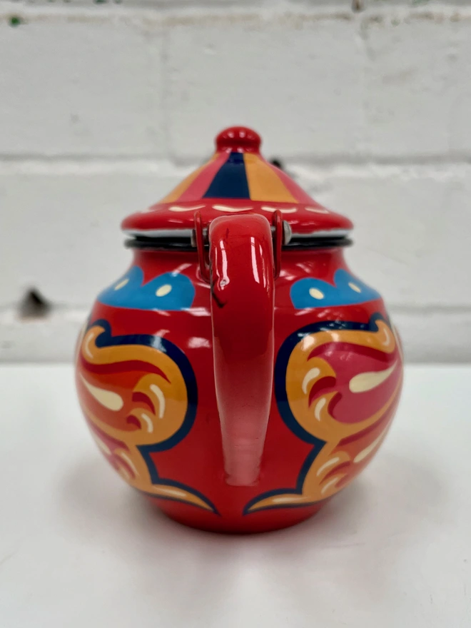 Small red vintage enamel teapot, hand painted with a traditional fairground inspired design in pink, orange and yellow. Teapot has a hinged lid.