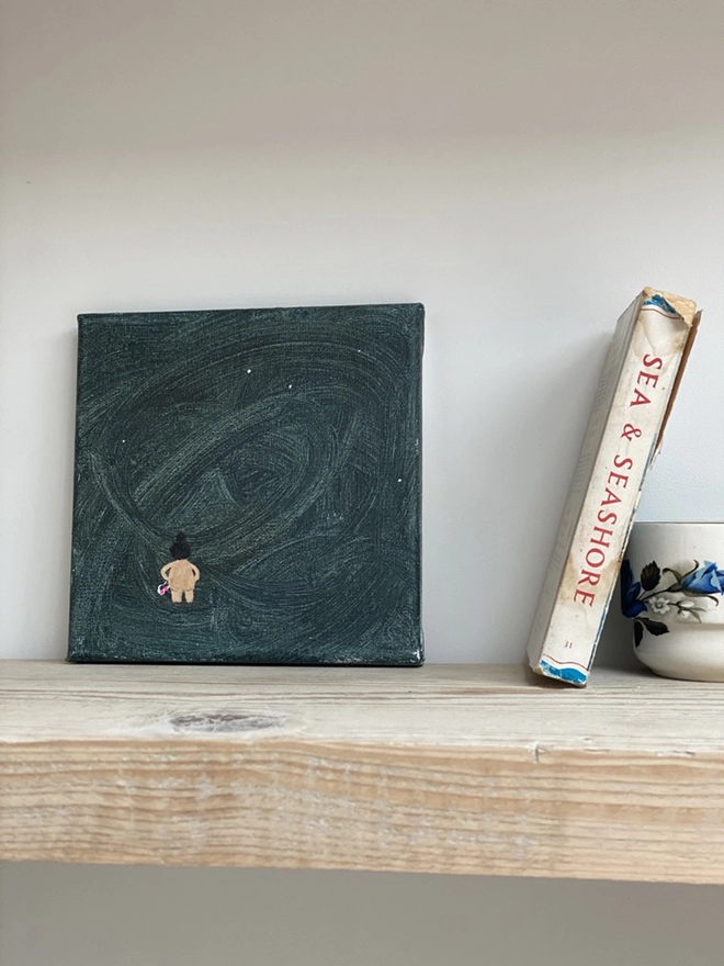 pale wooden shelf with small canvas painting with dark blue background and nude swimmer with pink goggles
