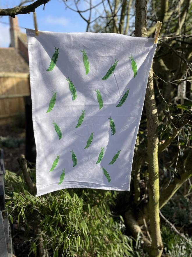 Pea Kitchen Tea Towel. White fabric with a diagonal pattern of green pea pods, some open to show bright green peas.