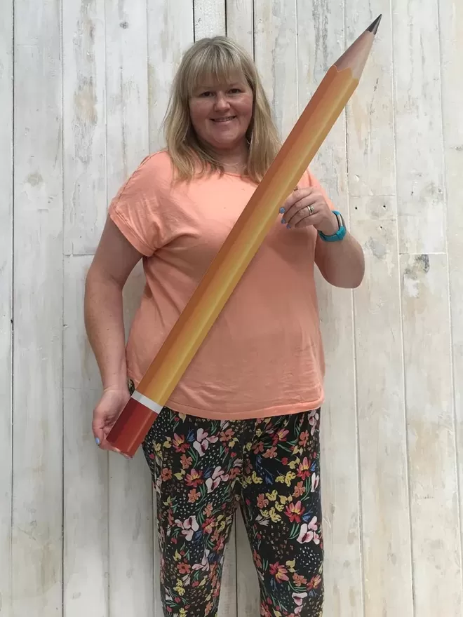 Giant Pencil seen held by a woman wearing floral trousers.