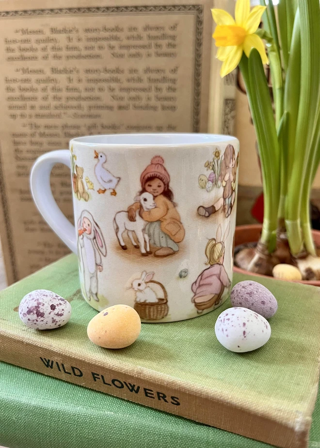 ceramic childrens mug featuring hand drawn vintage style illustrations of Easter images, a child hugging a lamb, easter eggs, a child dressed as a bunny