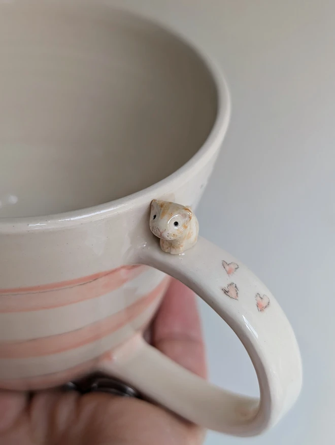 pottery cup with pink stripes and a tiny ceramic cat on the handle